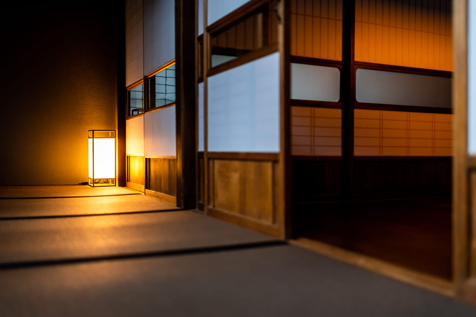 A single paper lantern glowing in a darkened ryokan corridor, tatami floor and sliding screens lit warm against the night