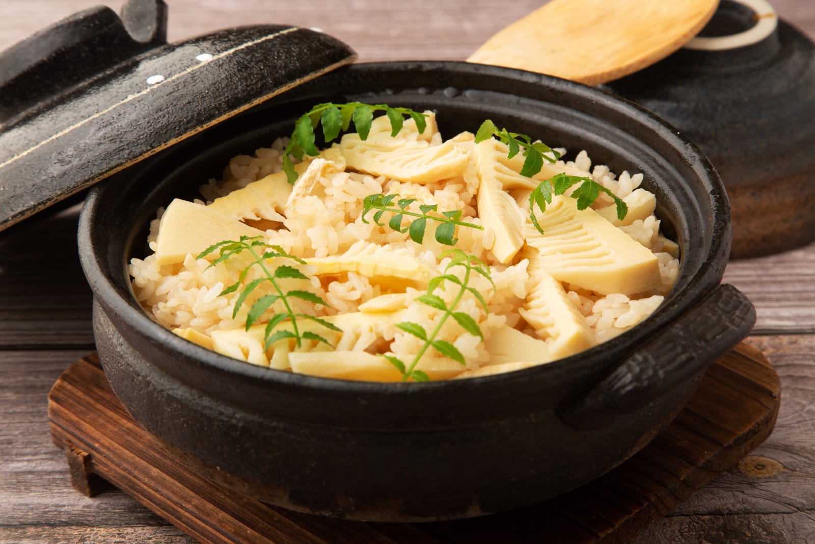 Bamboo shoot and rice in a black clay pot, garnished with sprigs of kinome, the young leaf of the sanshō tree