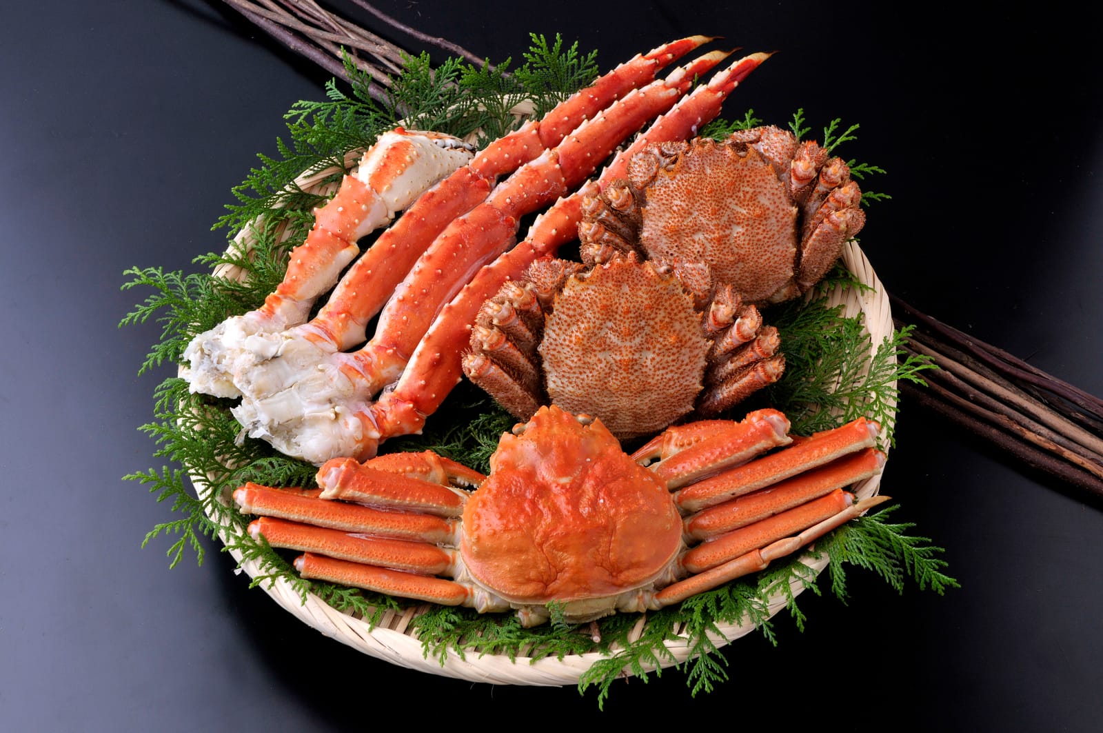 King crab, hairy crab and snow crab arranged together on a woven tray with cedar sprigs