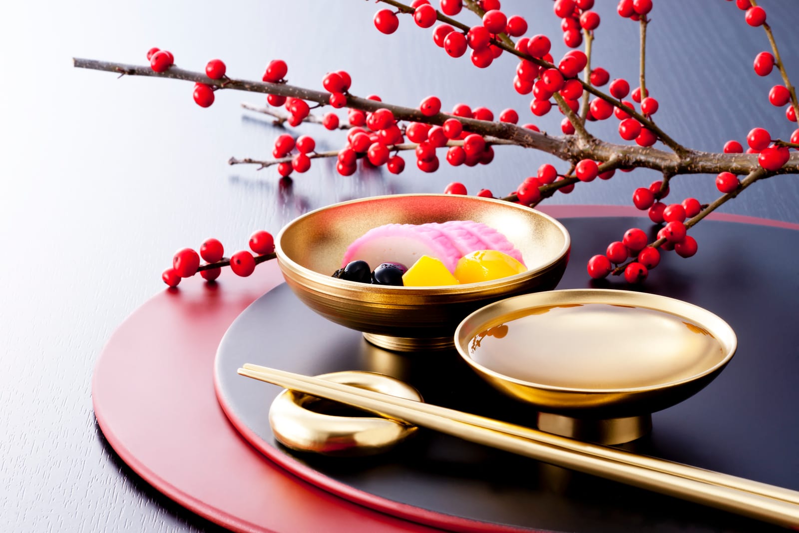 A small gold lacquer bowl and matching plate on a black and red lacquer tray, gold chopsticks resting beside them