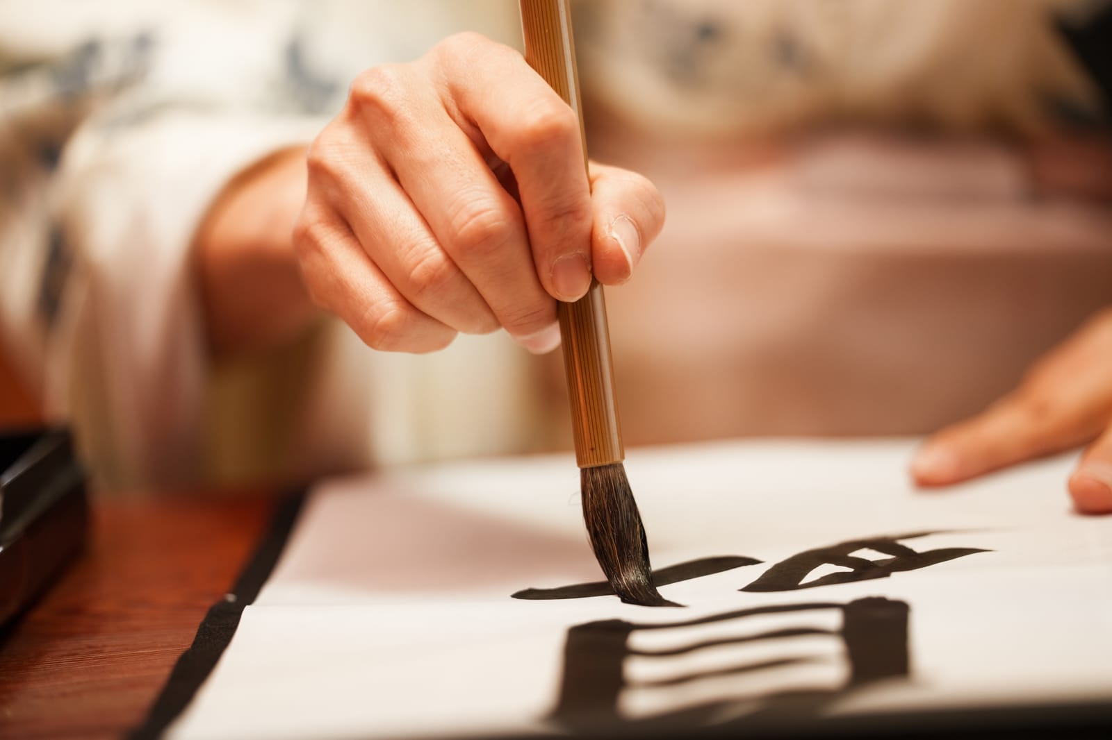 A hand guiding a bamboo brush across paper, forming a bold black calligraphy stroke