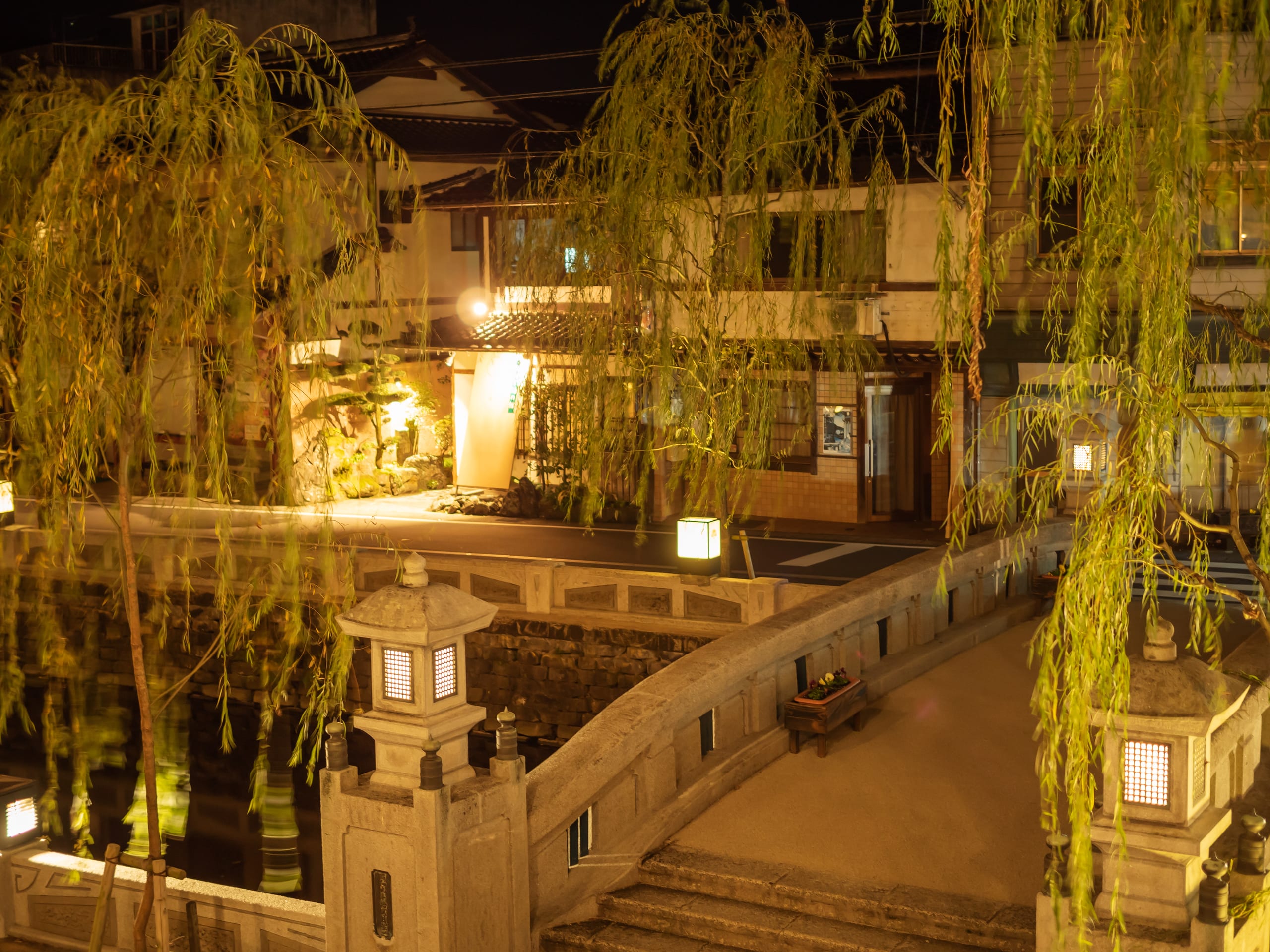 Kinosaki Onsen's canal lit by lanterns after dark, willows overhead