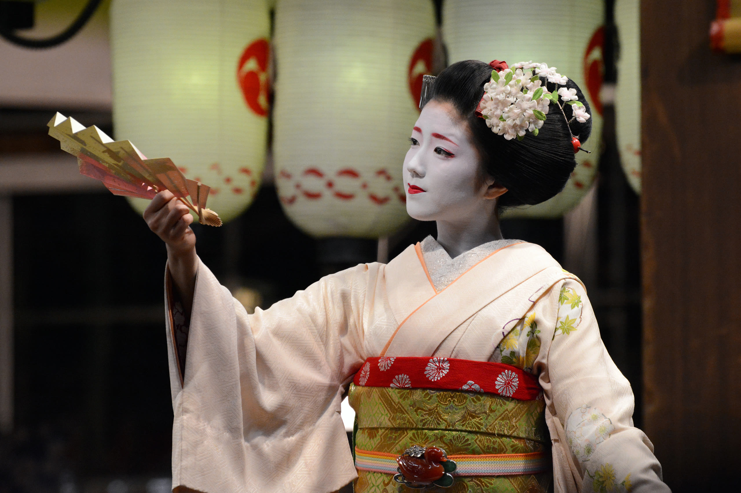 A maiko holding a folding fan in a Gion teahouse