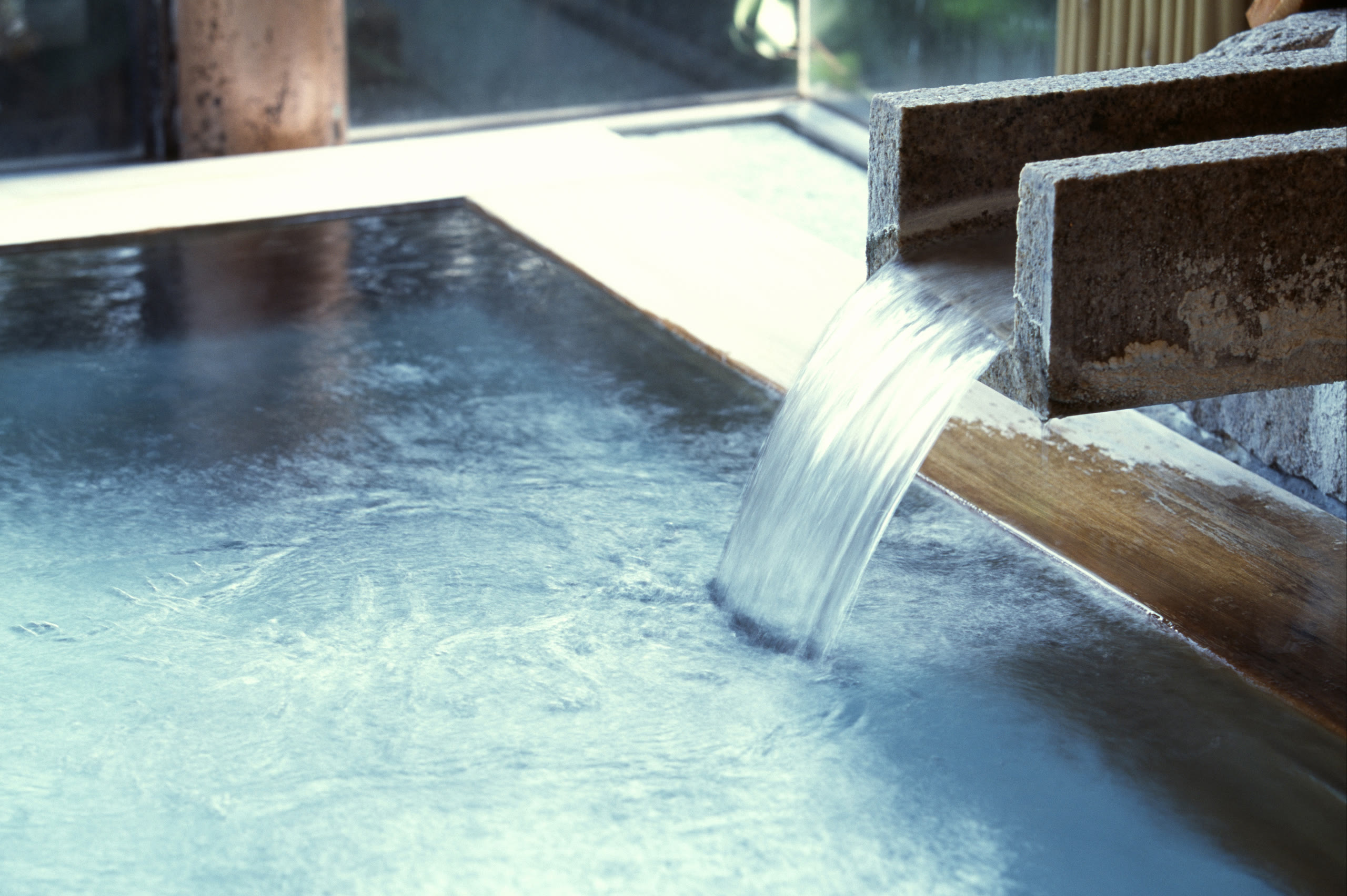 Hot spring water flowing from a bamboo spout into an onsen bath