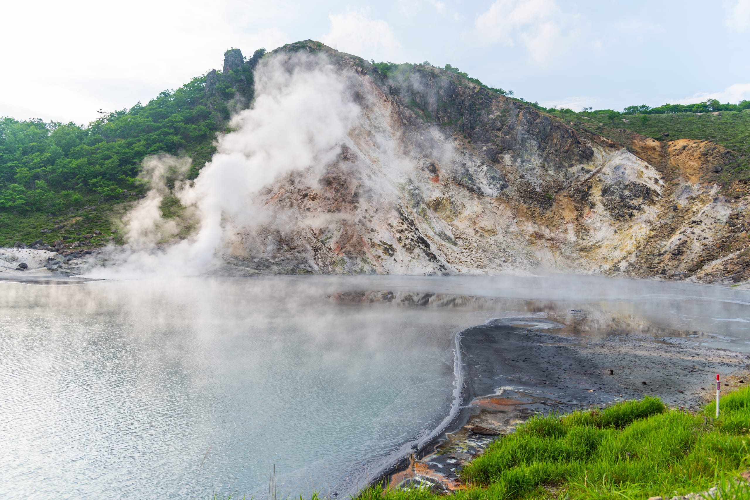 Steam lifting off the sulphurous crater pond at Oyunuma, Noboribetsu, the mineral slope bare above it